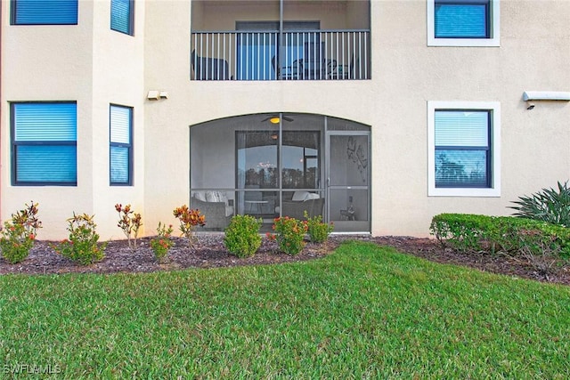 view of exterior entry featuring a balcony, a yard, and stucco siding