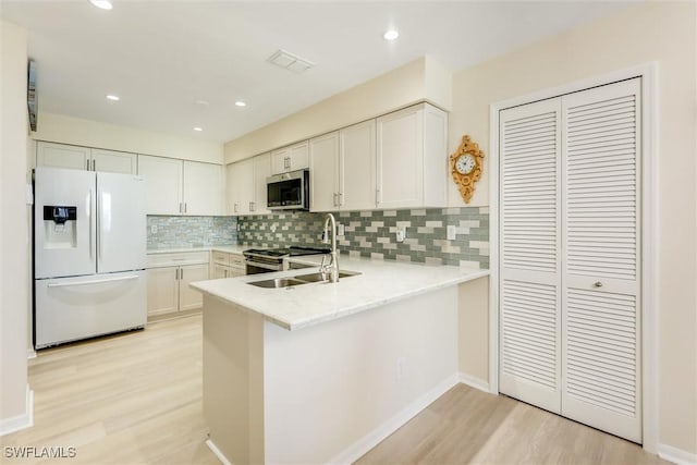 kitchen with tasteful backsplash, light wood-style flooring, appliances with stainless steel finishes, a sink, and a peninsula