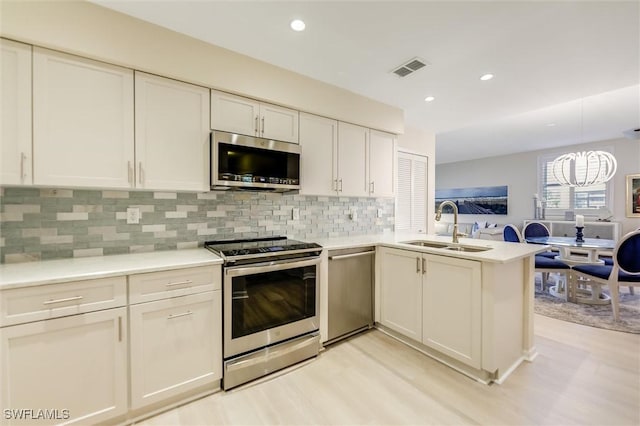 kitchen featuring visible vents, light countertops, appliances with stainless steel finishes, a sink, and a peninsula