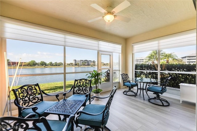 sunroom / solarium with a ceiling fan and a water view