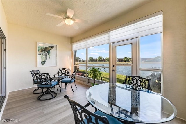 dining space featuring a water view, ceiling fan, a textured ceiling, and wood finished floors