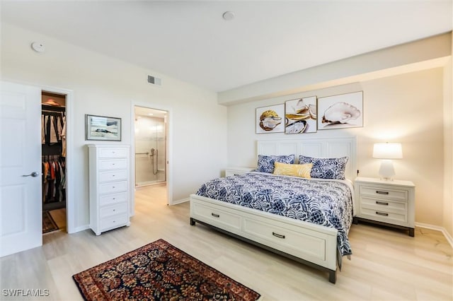 bedroom featuring baseboards, visible vents, connected bathroom, light wood-style flooring, and a spacious closet