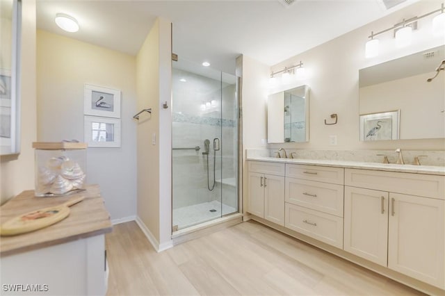 bathroom with double vanity, a stall shower, a sink, and wood finished floors