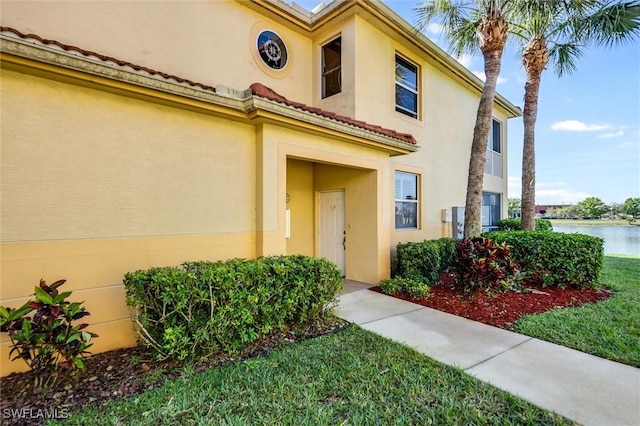 property entrance featuring a water view, stucco siding, and a lawn