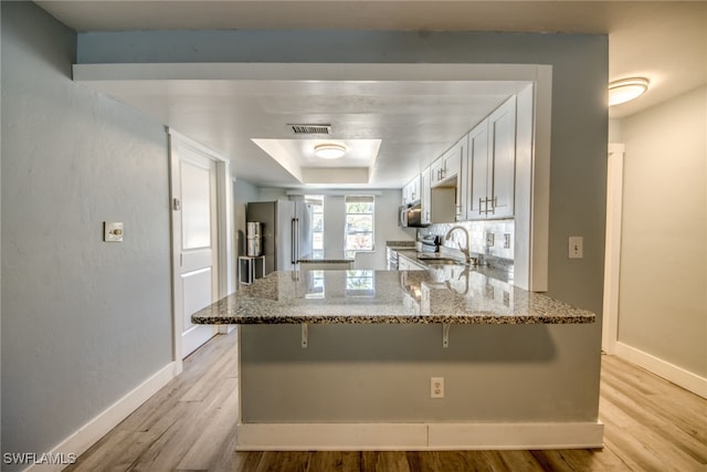 kitchen featuring stone countertops, visible vents, a raised ceiling, a peninsula, and light wood-type flooring