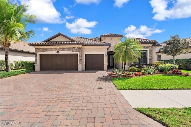 mediterranean / spanish house with decorative driveway, stucco siding, a garage, stone siding, and a tiled roof