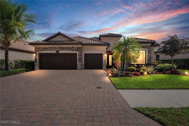 mediterranean / spanish home with stone siding, a tiled roof, an attached garage, decorative driveway, and stucco siding