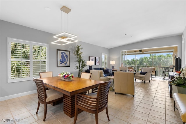 dining space with ceiling fan with notable chandelier, vaulted ceiling, baseboards, and light tile patterned floors