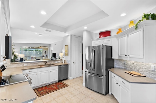 kitchen with appliances with stainless steel finishes, a tray ceiling, white cabinets, and a sink