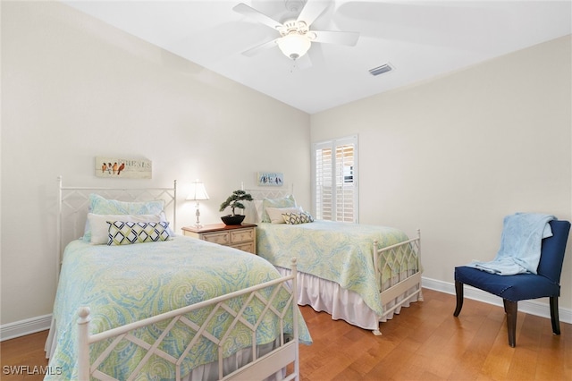 bedroom featuring a ceiling fan, wood finished floors, visible vents, and baseboards