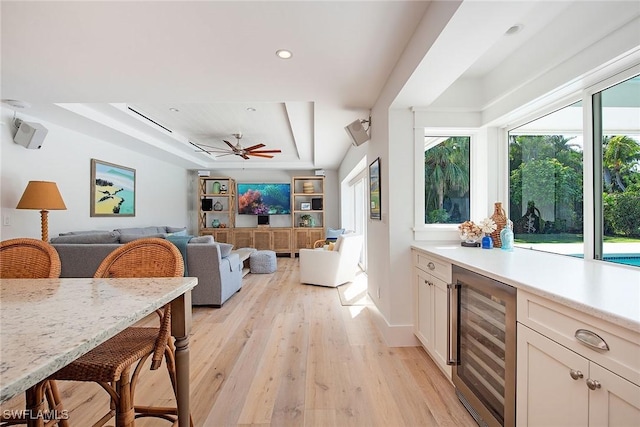 kitchen featuring a tray ceiling, light countertops, light wood-style floors, open floor plan, and beverage cooler