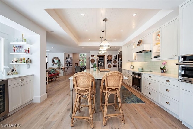 kitchen with open shelves, a tray ceiling, a sink, and stainless steel oven