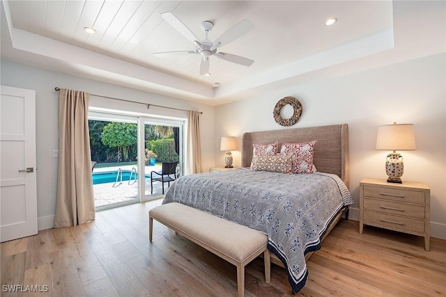 bedroom featuring access to outside, a raised ceiling, baseboards, and light wood finished floors