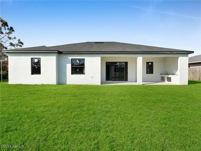 rear view of house with a patio, an outdoor kitchen, a shingled roof, a lawn, and stucco siding