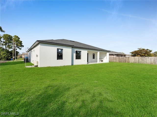 rear view of house featuring central AC unit, stucco siding, fence, and a yard