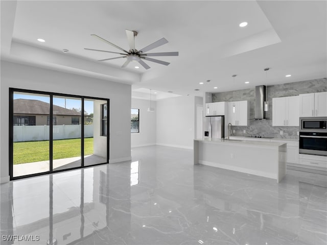 kitchen with wall chimney exhaust hood, open floor plan, stainless steel appliances, light countertops, and white cabinetry