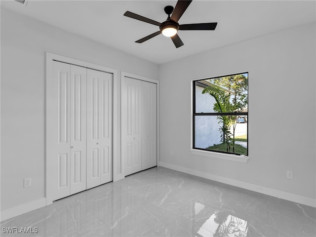 unfurnished bedroom featuring marble finish floor, ceiling fan, baseboards, and two closets