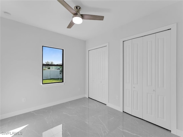 unfurnished bedroom featuring a ceiling fan, marble finish floor, baseboards, and two closets