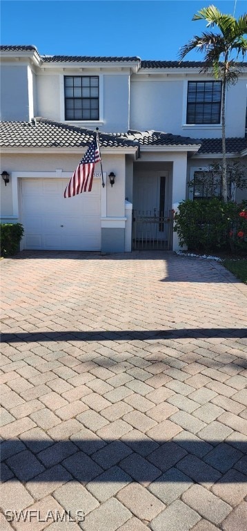 view of property with a garage, decorative driveway, a tile roof, and stucco siding