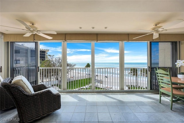 sunroom / solarium with a water view, a ceiling fan, and a view of the beach