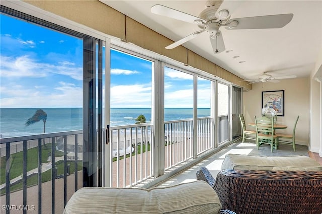 sunroom with a ceiling fan, a view of the beach, and a water view