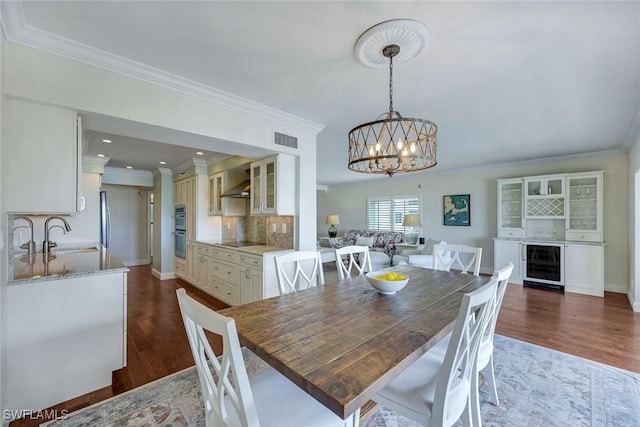 dining space featuring wine cooler, crown molding, visible vents, dark wood-type flooring, and a chandelier