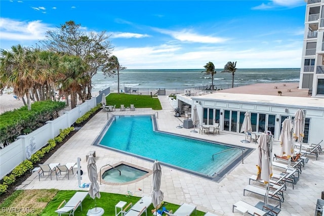 pool with a patio area, fence, a hot tub, and a water view