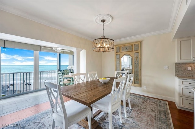 dining room with a water view, crown molding, baseboards, and wood finished floors