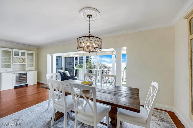 dining area featuring beverage cooler, ornamental molding, wood finished floors, and baseboards