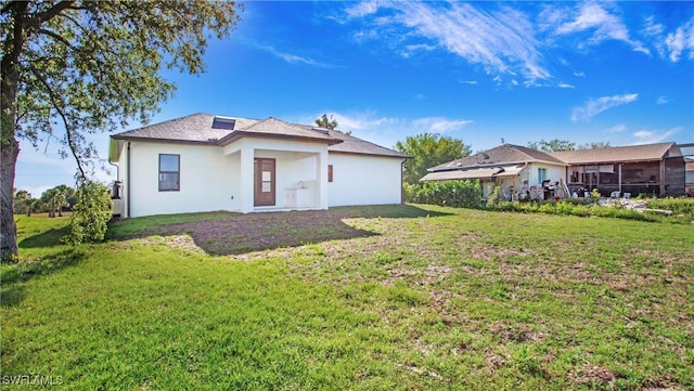 back of property featuring a lawn and stucco siding