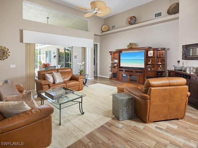 living area featuring light wood-style floors, ceiling fan, a high ceiling, and visible vents