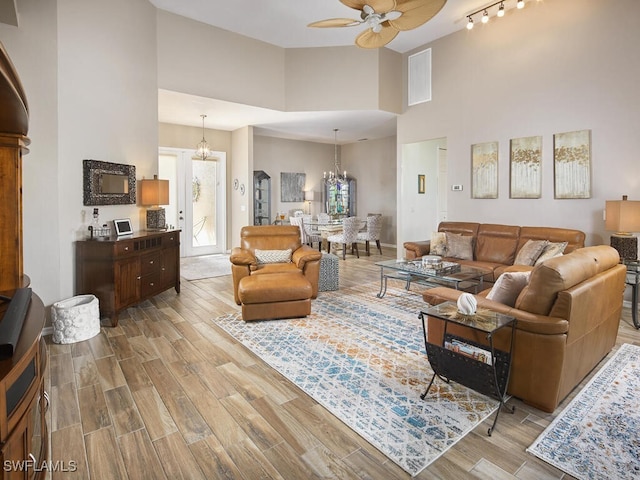 living room featuring baseboards, a high ceiling, ceiling fan with notable chandelier, and wood finish floors