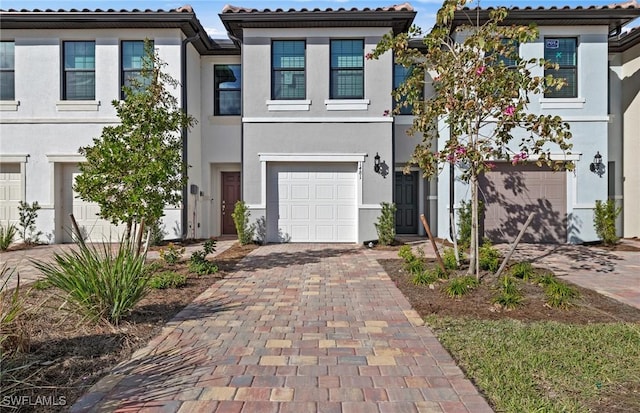 view of front of property with an attached garage, a tiled roof, decorative driveway, and stucco siding