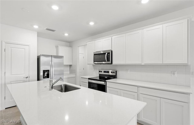 kitchen with stainless steel appliances, light countertops, white cabinetry, a sink, and an island with sink