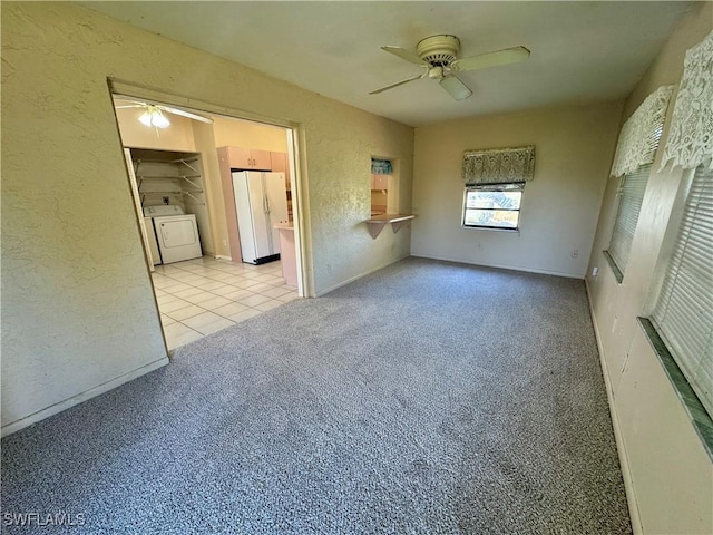 empty room featuring light carpet, a textured wall, washing machine and dryer, and a ceiling fan