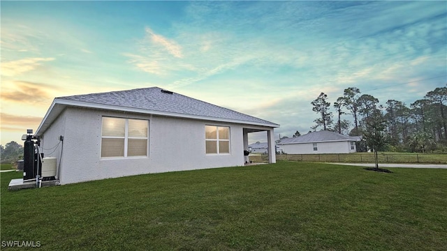 back of property with a shingled roof, a lawn, fence, and stucco siding