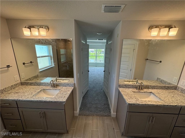 106 SE 5th Ave, Cape Coral, FL 33990 - bathroom featuring wood finish floors, two vanities, tiled shower, and a textured ceiling