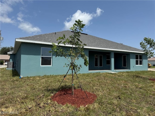 106 SE 5th Ave, Cape Coral, FL 33990 - back of house featuring stucco siding, central AC, a lawn, and roof with shingles
