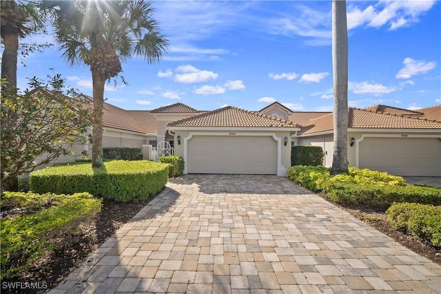 mediterranean / spanish house with decorative driveway, a tiled roof, an attached garage, and stucco siding