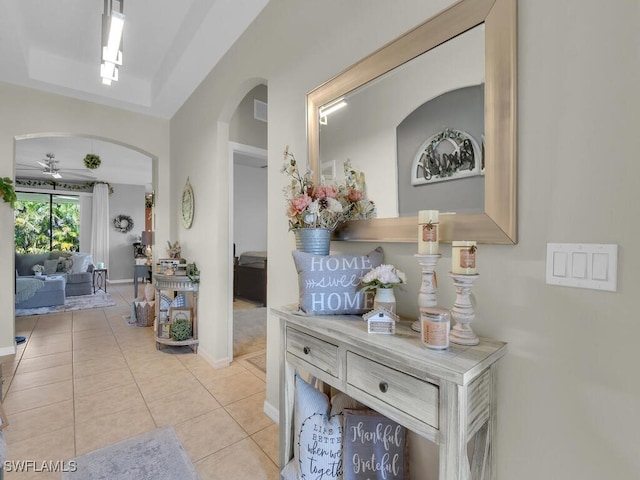 hallway with arched walkways, light tile patterned flooring, visible vents, baseboards, and a raised ceiling