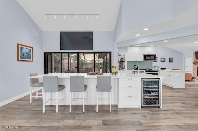 8080 Lagoon Rd, Fort Myers Beach, FL 33931 - bar area featuring beverage cooler, stainless steel microwave, high vaulted ceiling, rail lighting, and light wood finished floors