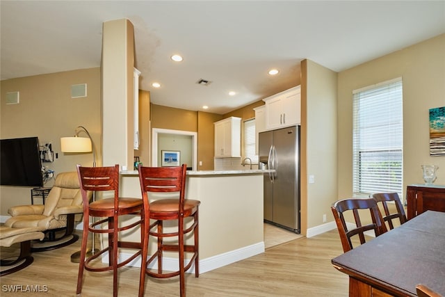 kitchen with visible vents, white cabinets, light countertops, a kitchen bar, and stainless steel refrigerator with ice dispenser