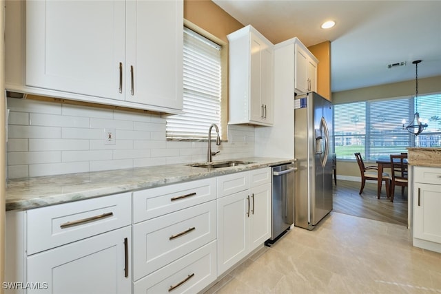 kitchen with a sink, white cabinetry, appliances with stainless steel finishes, light stone countertops, and decorative light fixtures