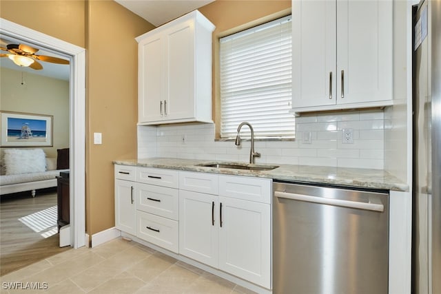 kitchen featuring stainless steel appliances, a sink, white cabinetry, light stone countertops, and tasteful backsplash