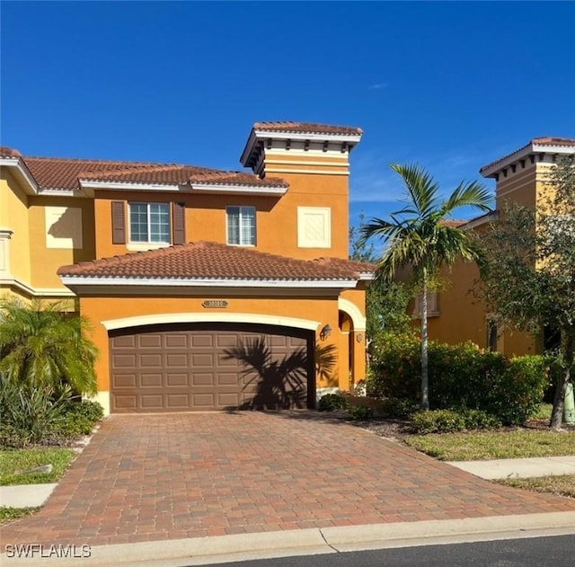 mediterranean / spanish home featuring a garage, decorative driveway, a tile roof, and stucco siding