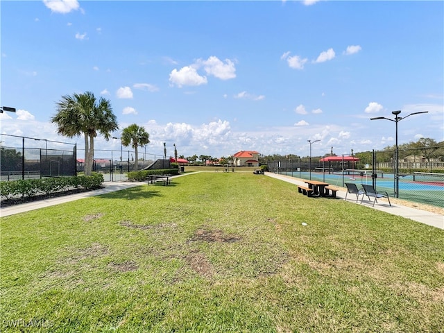 view of property's community with a yard, fence, and a tennis court