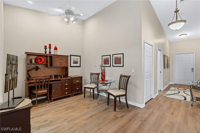 living area featuring baseboards, ceiling fan, light wood-style flooring, and a high ceiling