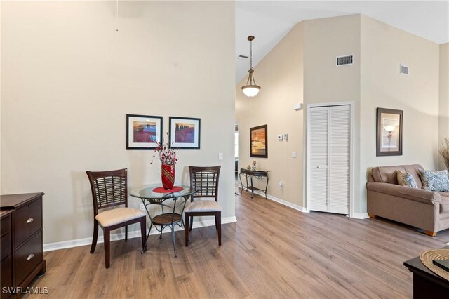 living area featuring high vaulted ceiling, light wood-style flooring, visible vents, and baseboards