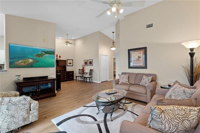 living area featuring a ceiling fan, light wood-type flooring, visible vents, and a towering ceiling