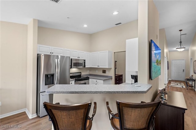 kitchen with a breakfast bar area, stainless steel appliances, a peninsula, white cabinetry, and light wood finished floors